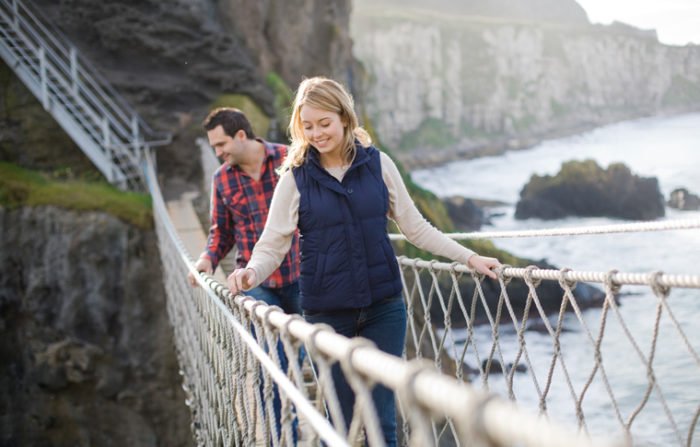 Couple look over edge while crossing carrick-a-rede rope bridge