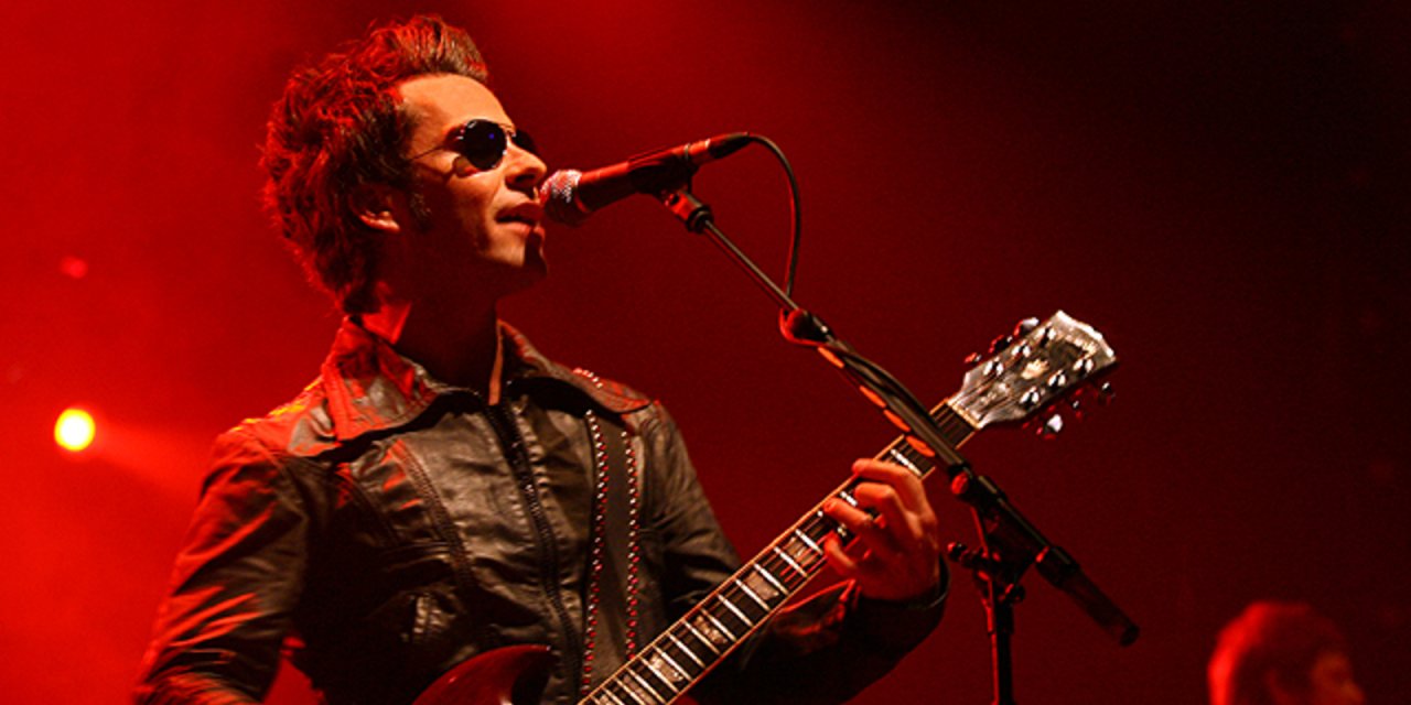 Man wearing black sunglasses singing into microphone with red led lights on stage
