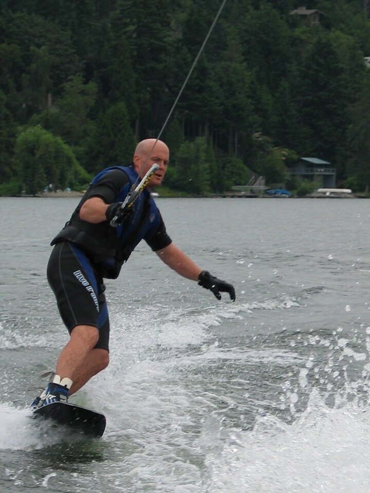 water,surfboarding, middle aged man, green trees, gloves on hand, watrsport