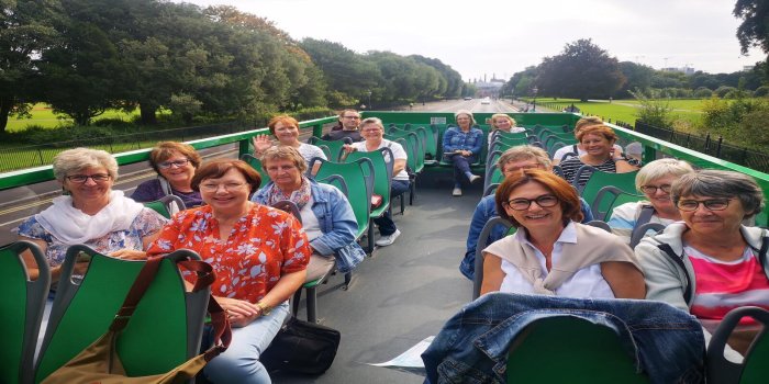 German Tour, Phoenix Park Top deck of Green Tour bus with 16 people spread across sitting on the seats. Green park with tall trees in the background.