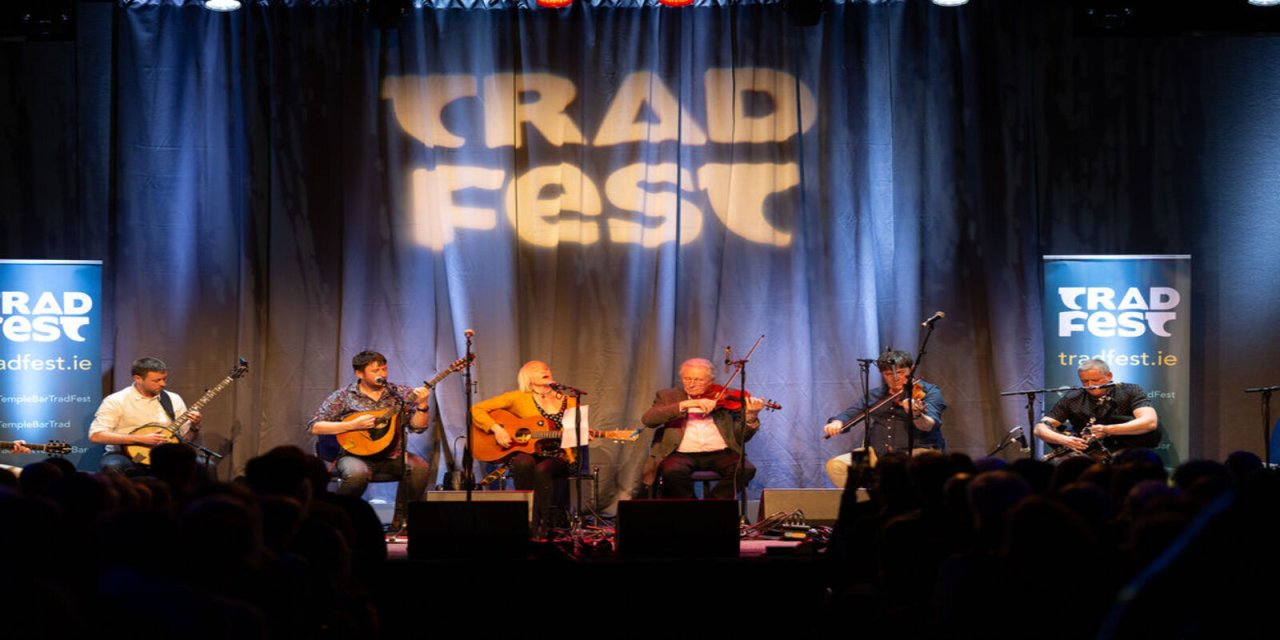 Dark stage with people sitting on stools playing traditional Irish instruments 