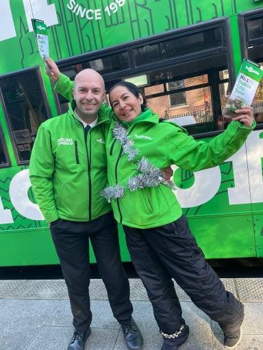 two people wearing green jackets posing outside a bus