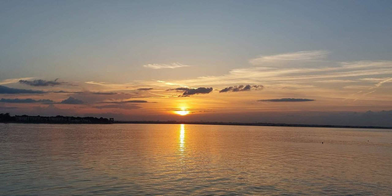 Bay of water with orange hue reflecting onto sea. Ombre sunset with a mixture of light and dark clouds in the sky.