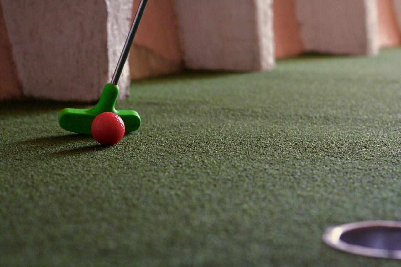 green putter, fake grass, orange ball. mini golf, orange wall 