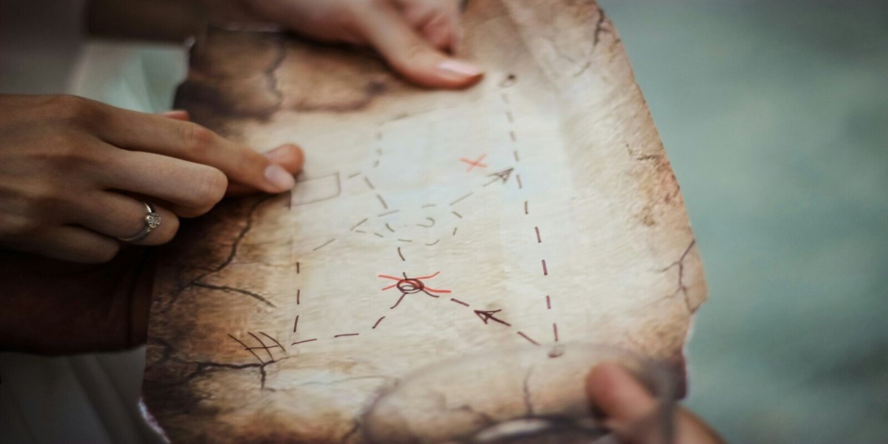 Ripped old brown map with 'x' marked. Girls hand holding map