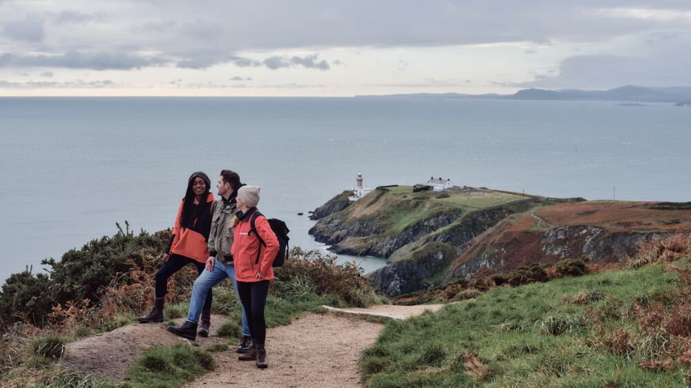 three people standing on a cliff path