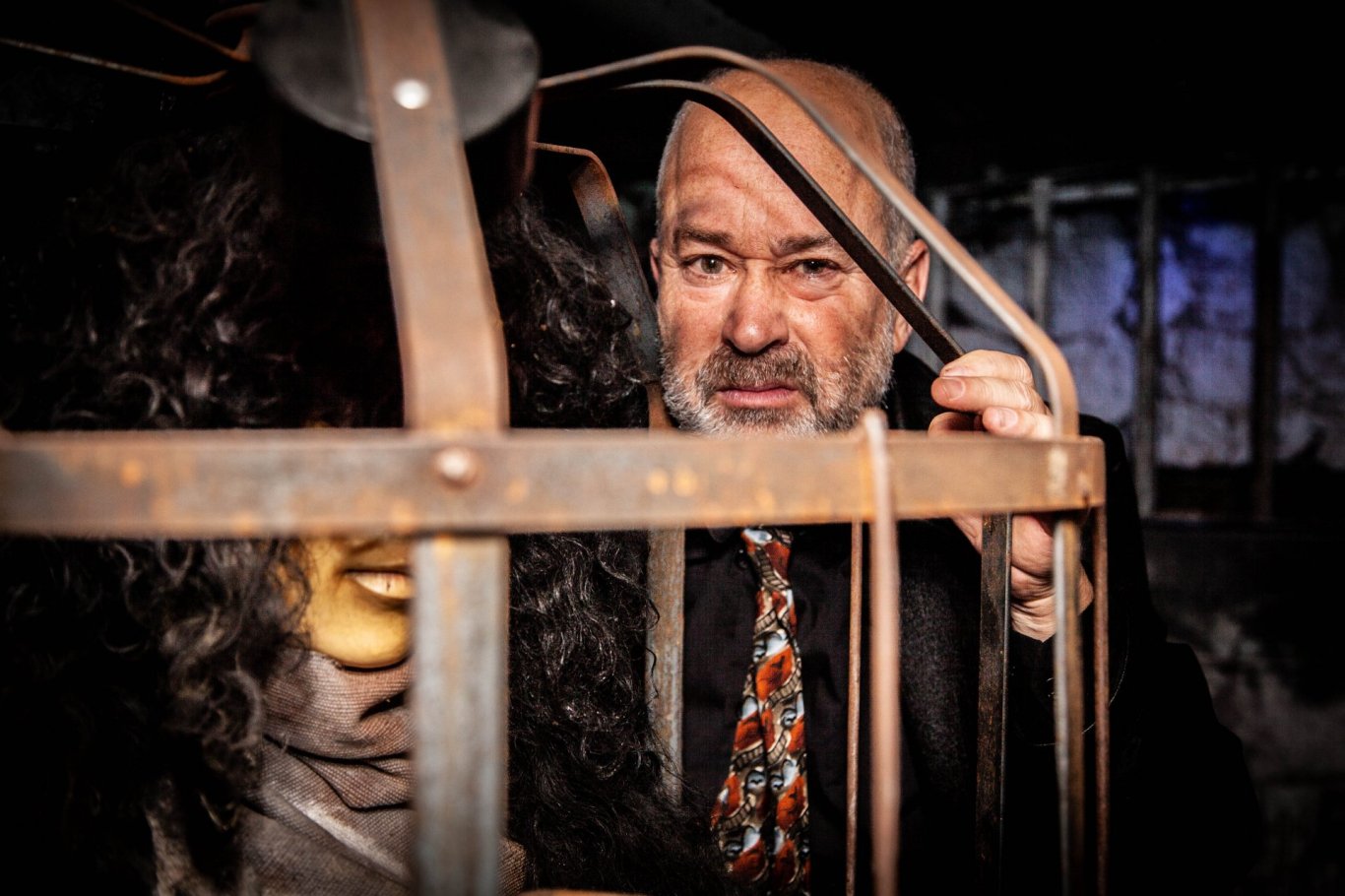 Image of man beside a cage with scary prop inside.