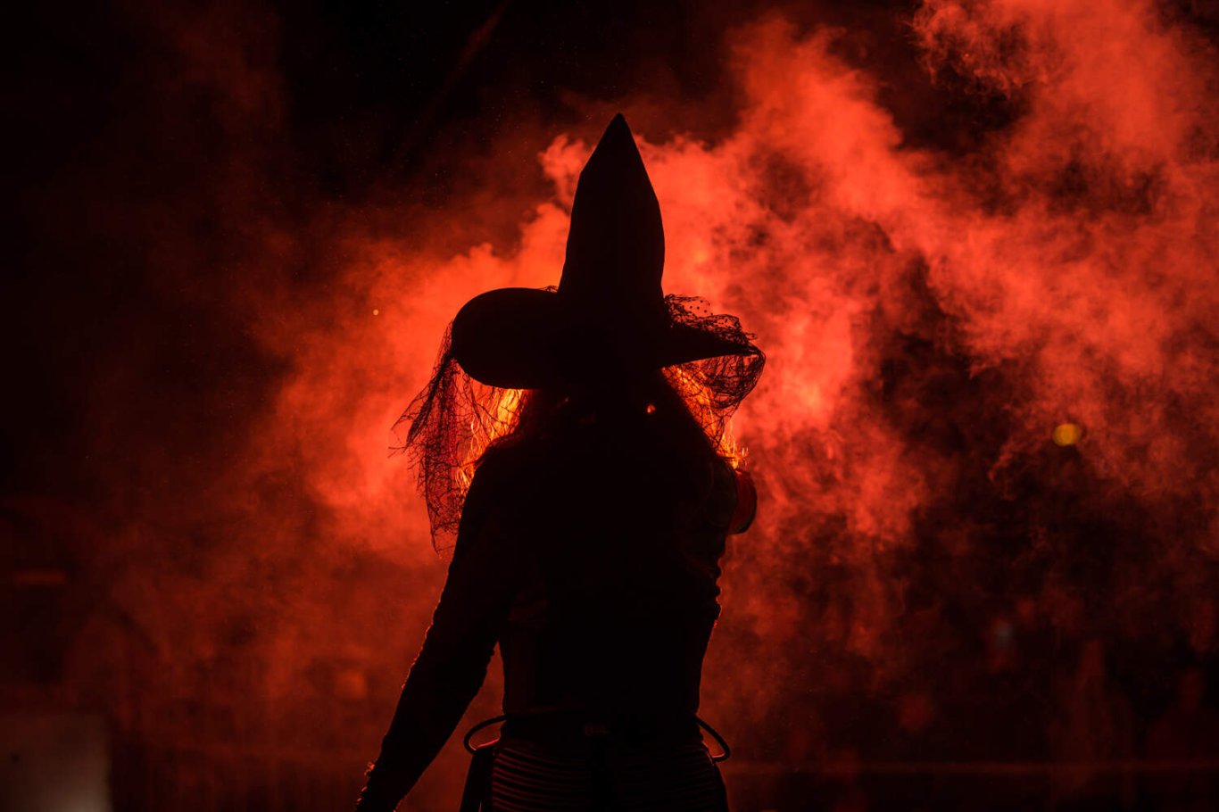 someone in a witches hat with red light and smoke behind them