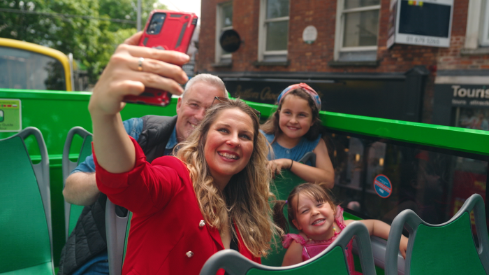 woman taking a picture of her family on top of the hop on hop off tour bus