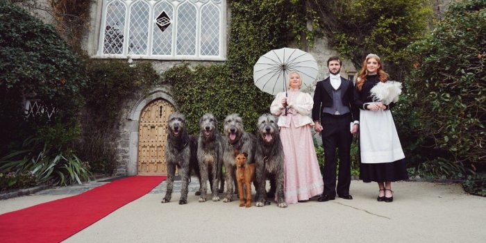 People holding two wolf hounds outside a castle