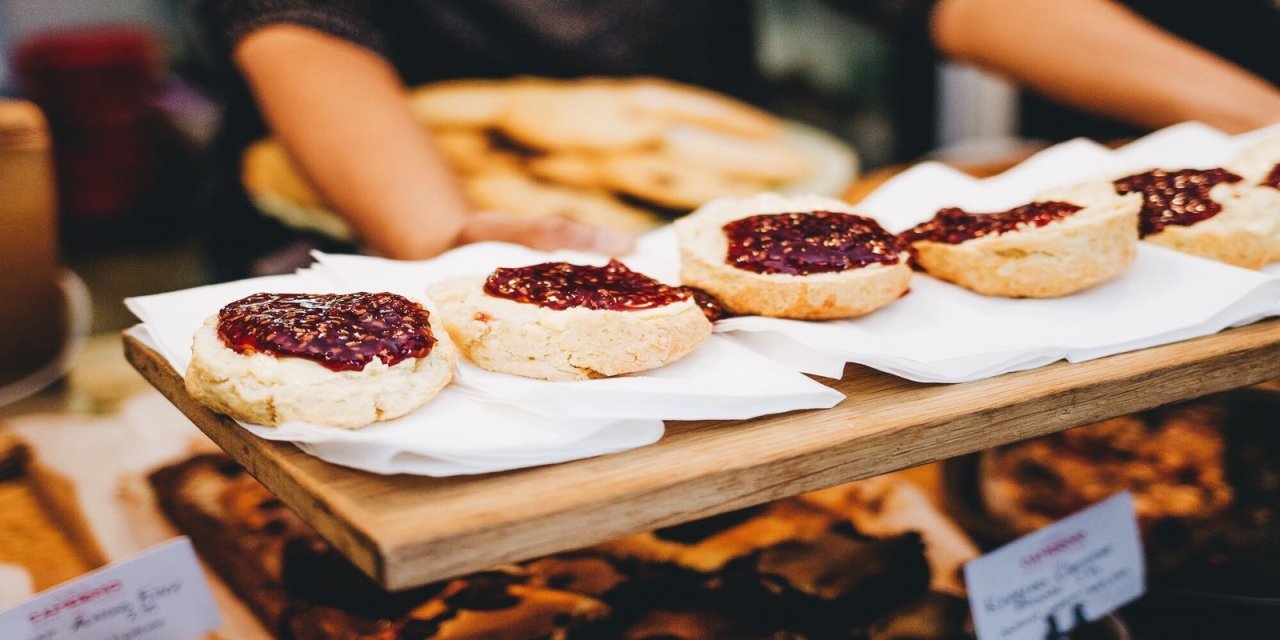 5 half scones with red jam spread on top sitting on white kitchen roll. They are presented on a wooden counter. 