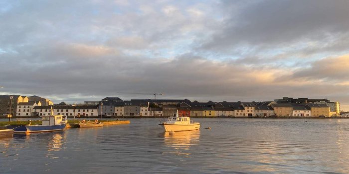 Courtesy Bernice Naughton, Fáilte Ireland, Sunset Walk Cloudy skies with orange sunset reflecting onto the blue water. White boat in the middle of the river with house landscape in the background