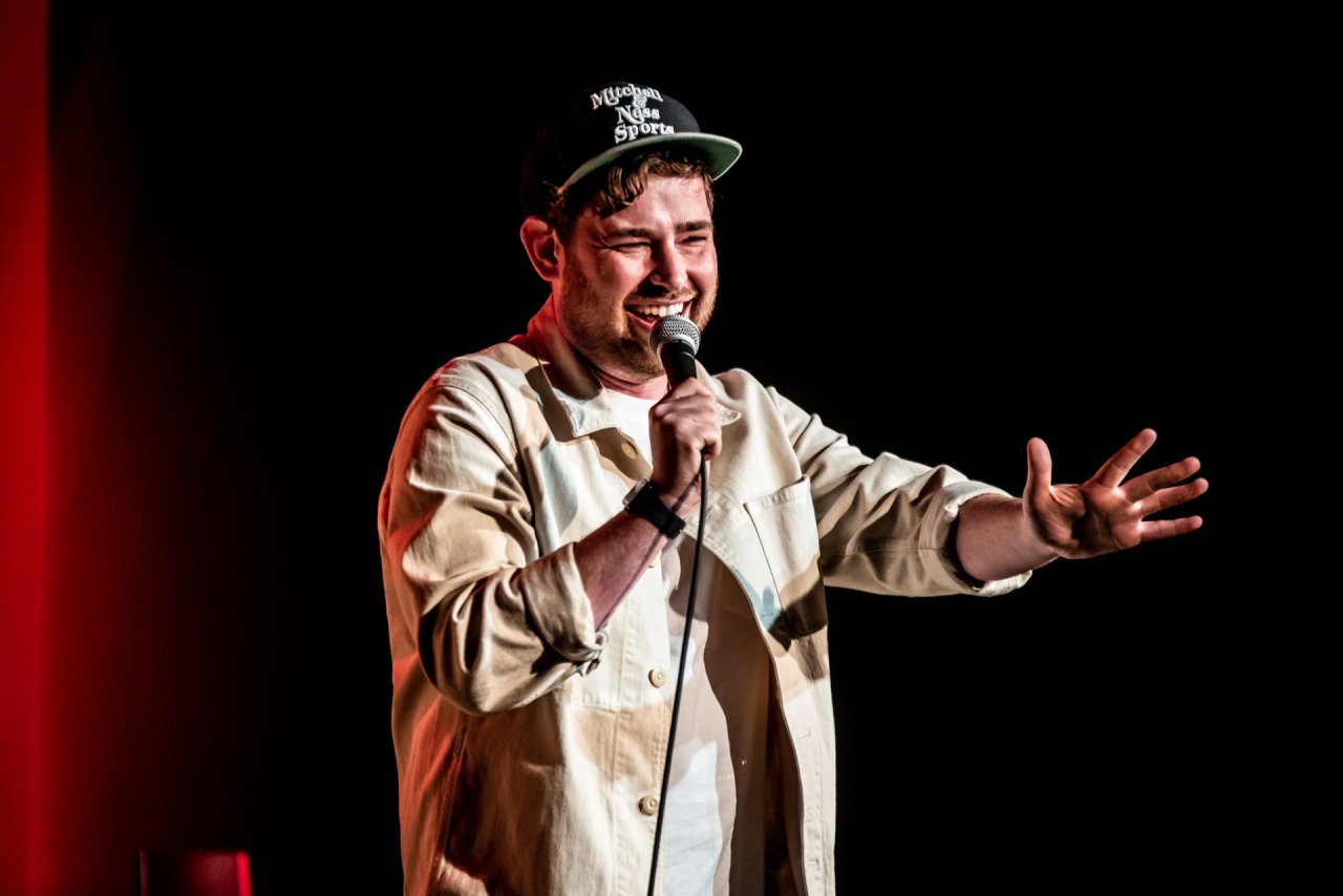 man on stage smiling while holding microphone