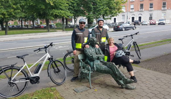 three people sitting on a bench beside a statue and bikes