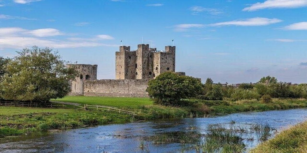 Trim stone castle surrounded by trees and bushes beside a blue lake 