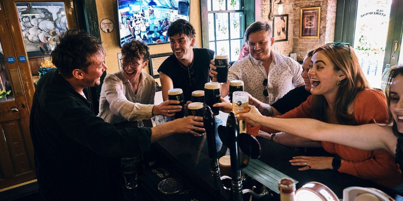 Group of people doing cheers holding Guinness, smiling and happy.