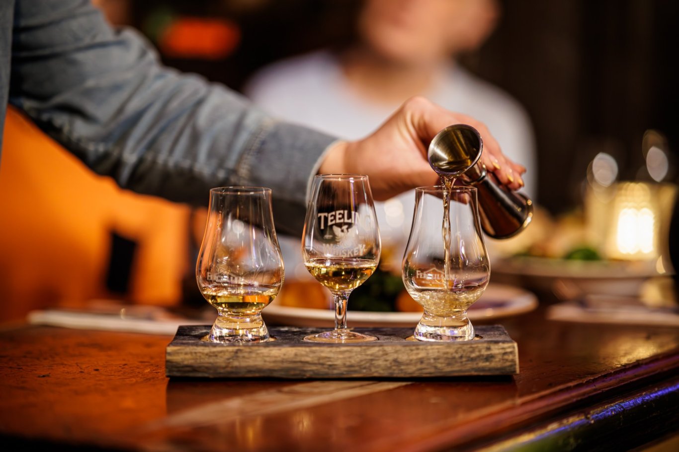 Whiskey Tour Pouring  hand-pouring-whiskey-3-glasses-blurred-background