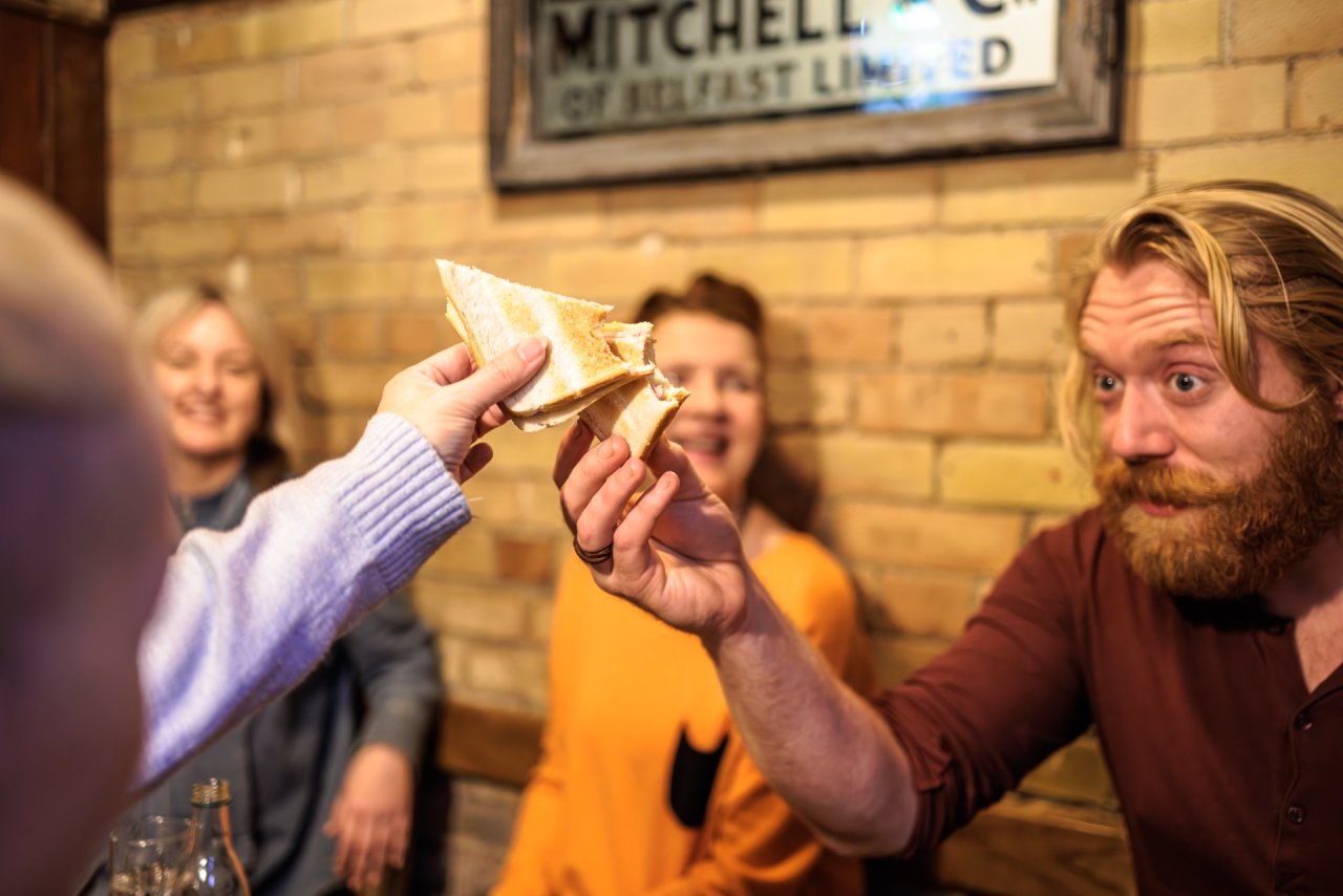 4 people-red-shirt-yellow-top-blonde-hair-toasted-sandwich-cheers-sign-on-wall-brick-wall
