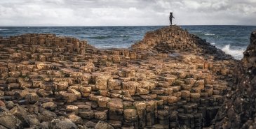 Person on giants causeway rocks while waves crash against shore