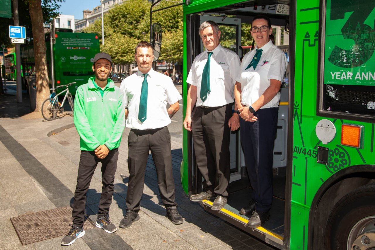 sales promoter standing beside three bus drivers, one standing on the ground the others on the entrance to the bus 