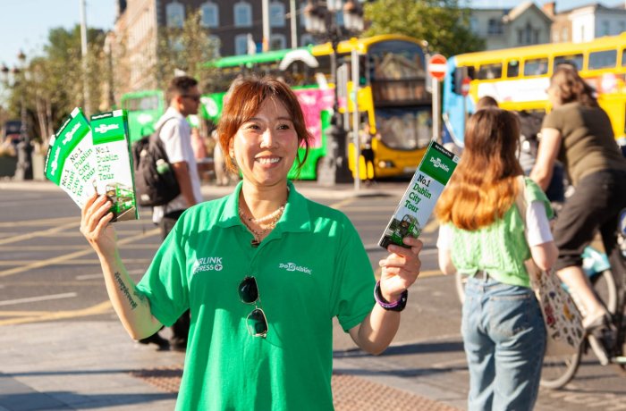 woman is smiling and standing on the street holding brochures