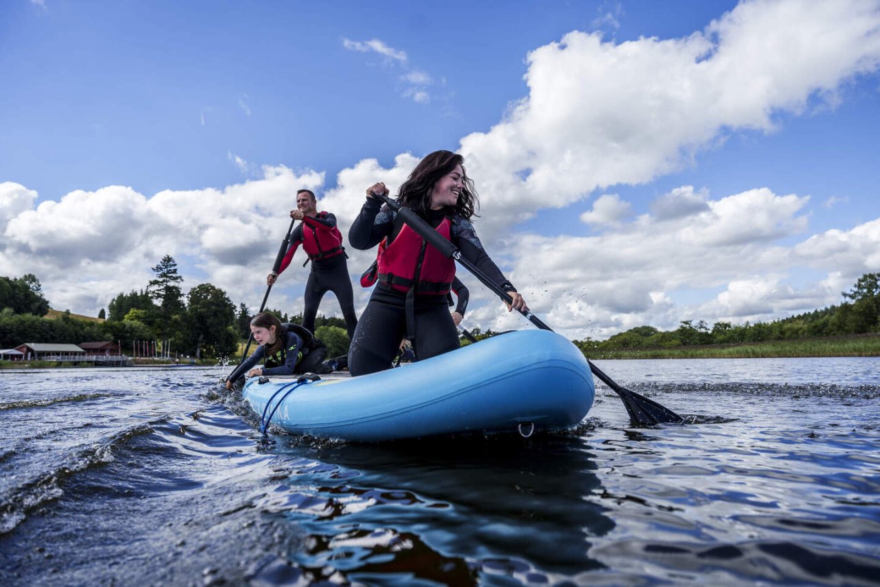 blue paddle board, family,red life jacket, smile,green trees